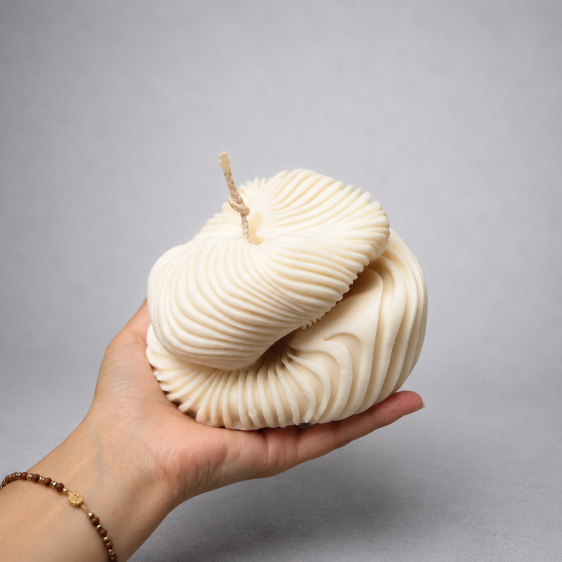 Hand holding the ivory Ethereal Fold Pillar Candle, showing its layered ribbed form and scale