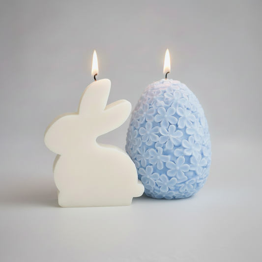 Candle-shaped bunny and egg on a plate with pastel-colored candles and flowers in the background
