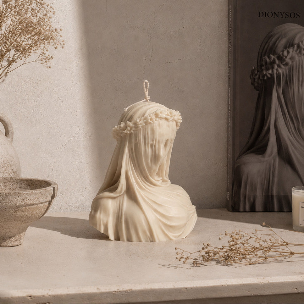 warm Warren London Veiled Vestal soy wax candle including a bust, vase with dried flowers, and candle on a shelf. 