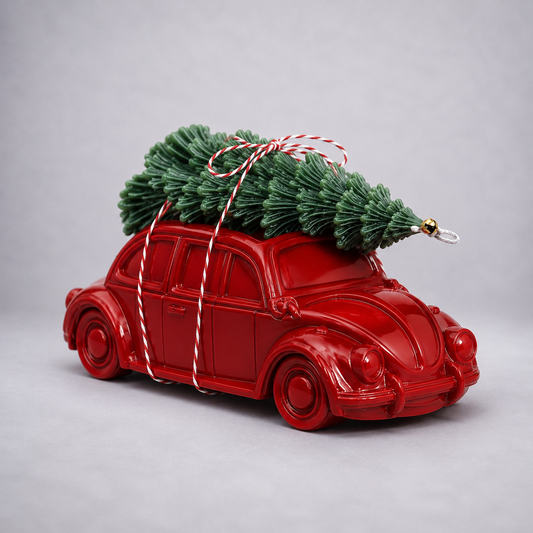 A glossy red toy Volkswagen Beetle car with a small green Christmas tree strapped on top, tied with red-and-white striped string, photographed on a light gray studio background. 