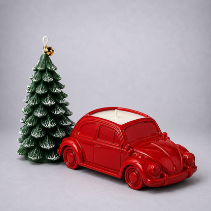 A red car-shaped candle with a white wax top and a small green Christmas tree ornament beside it, photographed on a plain light gray background.