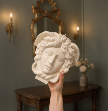 Hand holding a decorative head sculpture in a room with a mirror and candles. warm warren london handmade artisanal soy wax clean burn vegan large medusa bust candle 