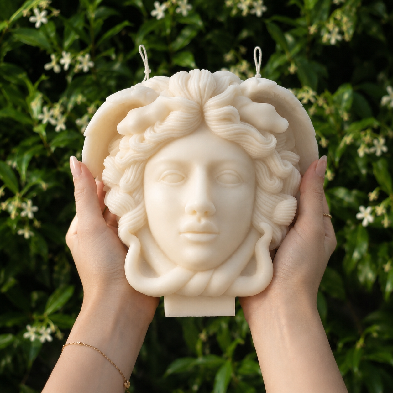Large ivory Medusa sculpture candle held in elegant hands in a blooming garden. Handmade luxury soy wax candle with intricate Greek mythology details and premium ivory finish, photographed in natural light.
